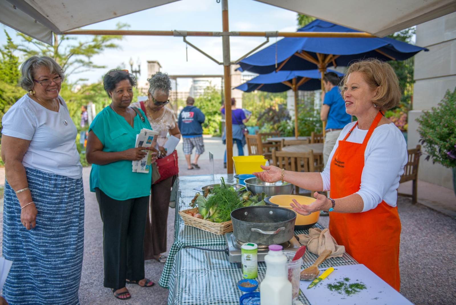 Three adult women look on as a USBG volunteer welcomes then to watch a cooking demonstration