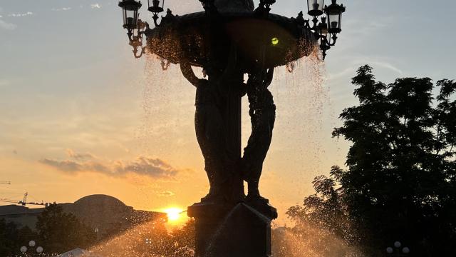 A 30 foot tall fountain sprays water with a golden sunset behind