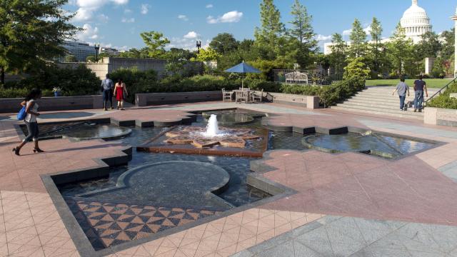 A large fountain with tile is surrounded by plants