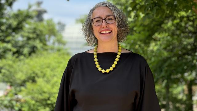 a woman in a black shirt stands amongst trees