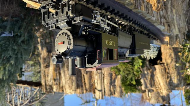 A black model train chugs along outdoor tracks under a blue sky