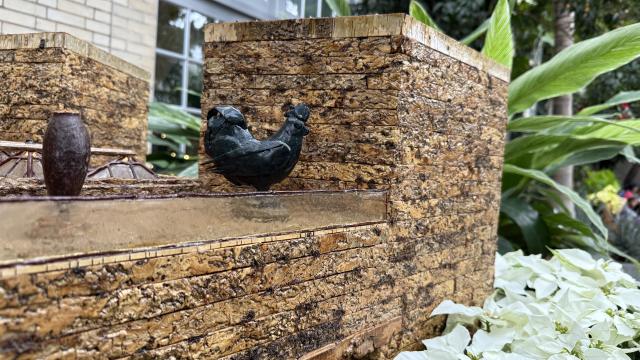 A 4" blue rooster model made from plant parts sit atop a model of the National Gallery of Art made from plant parts