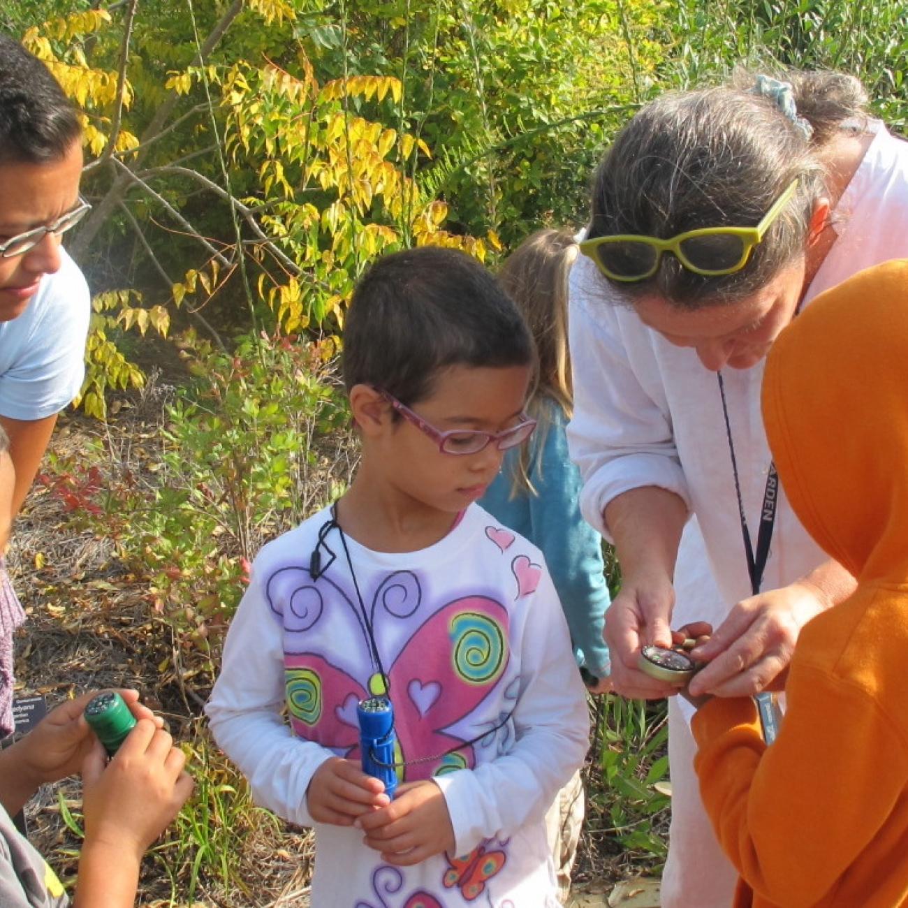 three young kids view a hand lens held by an instructor in an outdoor garden