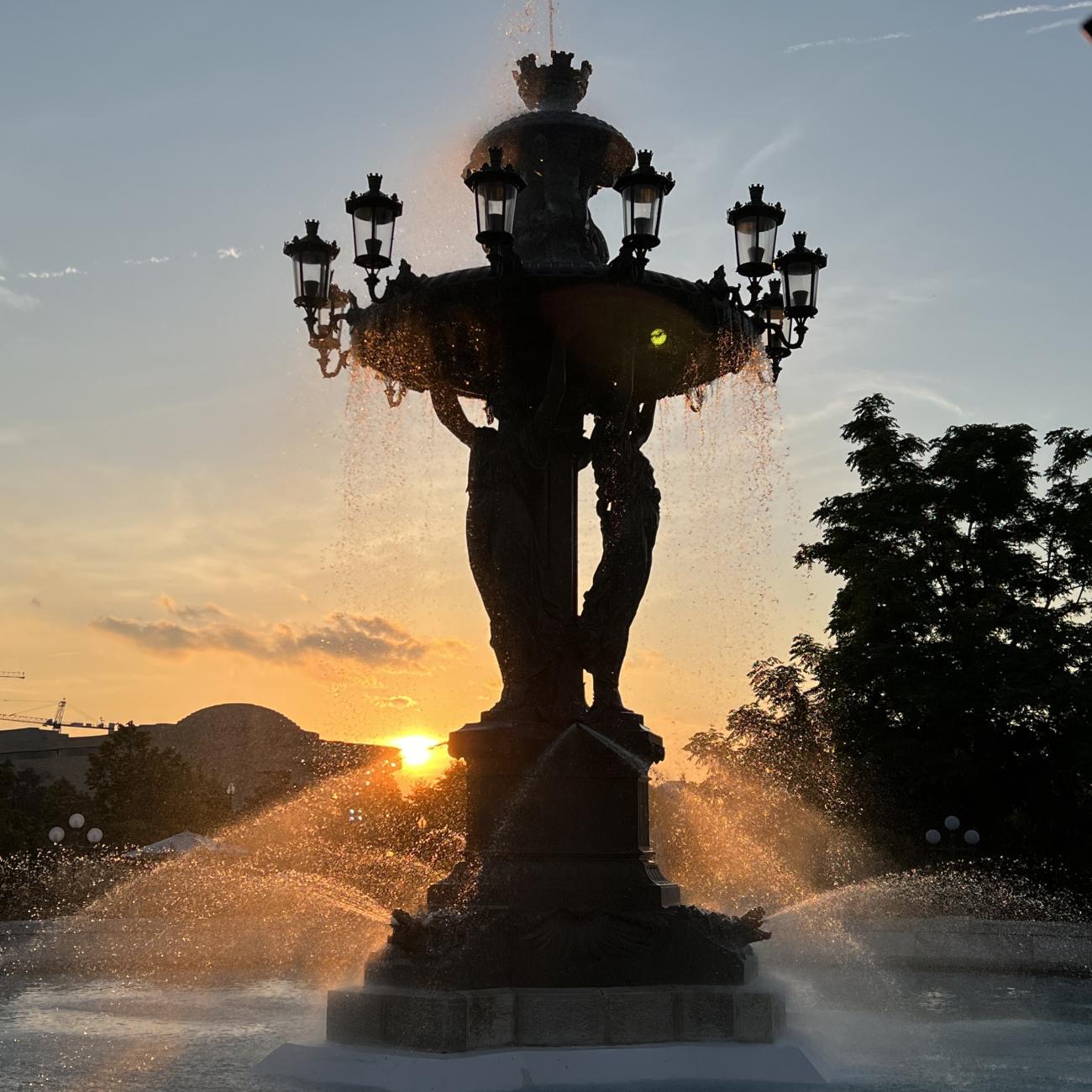 A 30 foot tall fountain sprays water with a golden sunset behind