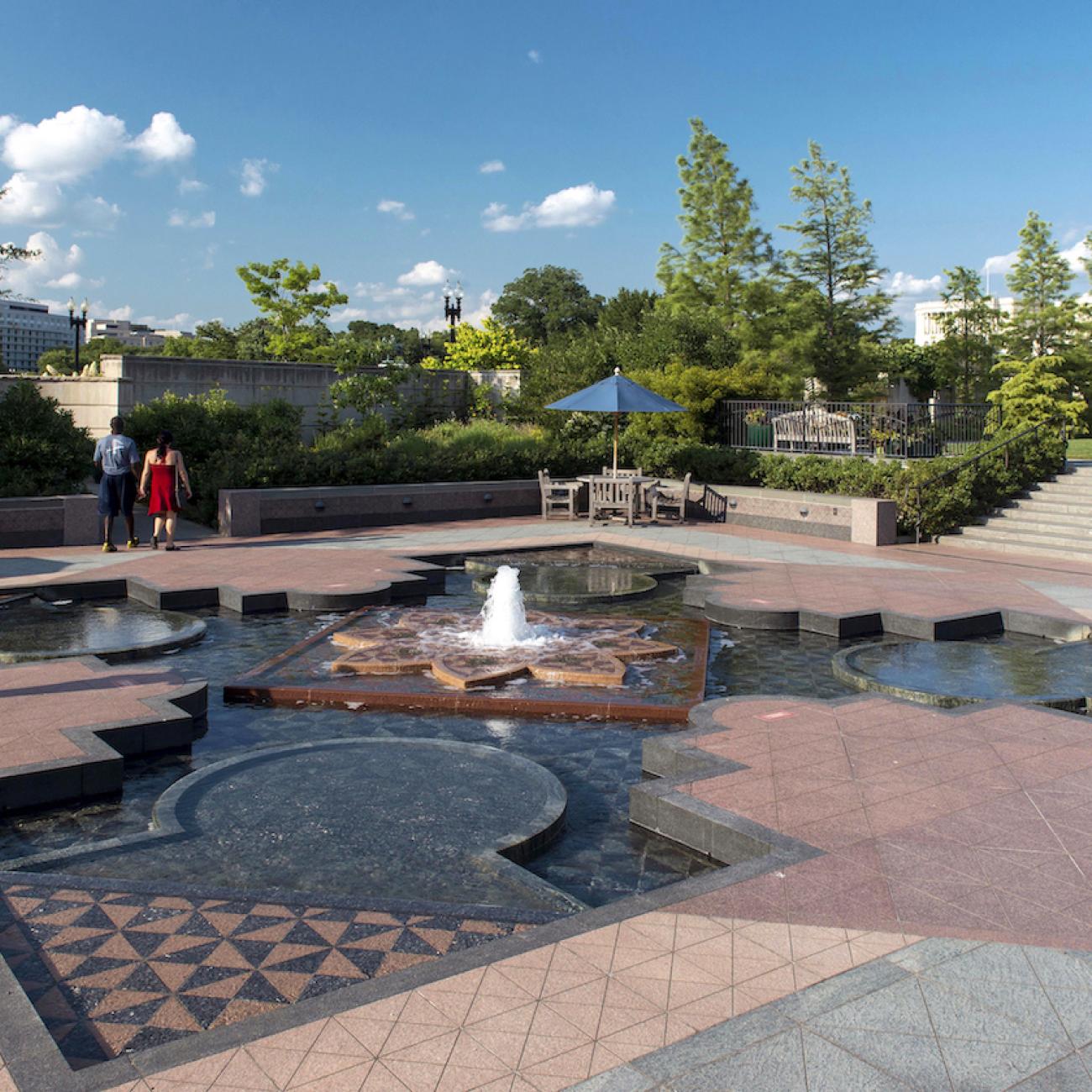 A large fountain with tile is surrounded by plants