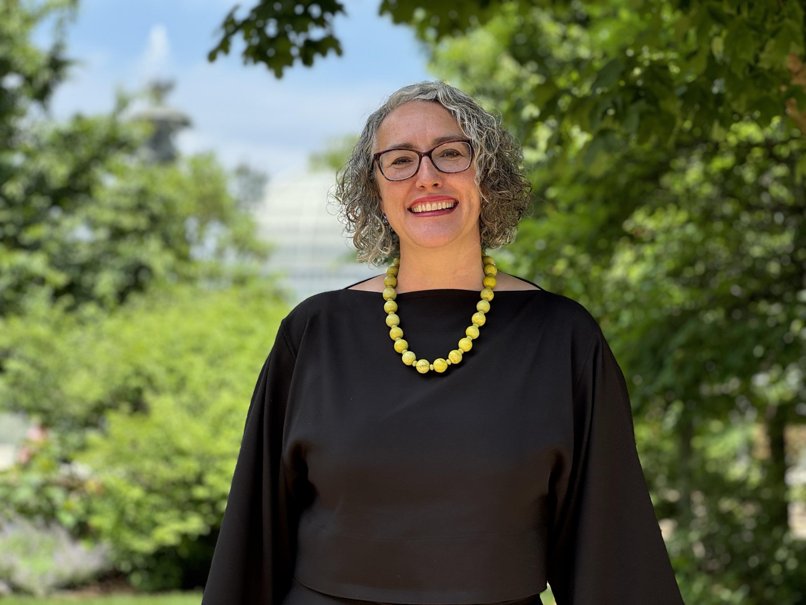 a woman in a black shirt stands amongst trees