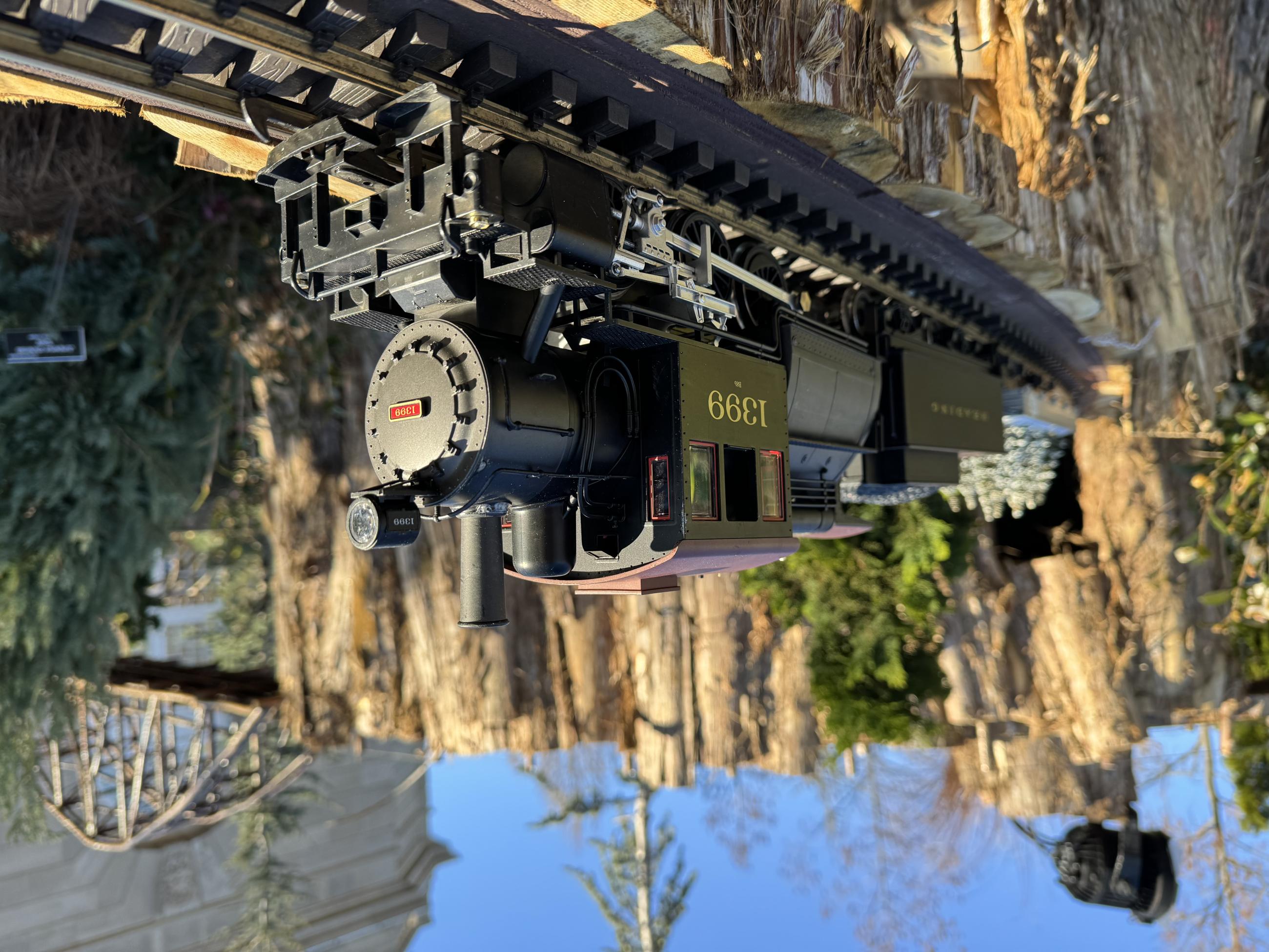 A black model train chugs along outdoor tracks under a blue sky